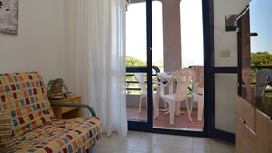 A balcony with a table and chairs, a sofa, and a sliding glass door leading to an outdoor area. - Soak Up the Sun Relaxing Apartment Near the Beach (San Michele al Tagliamento)