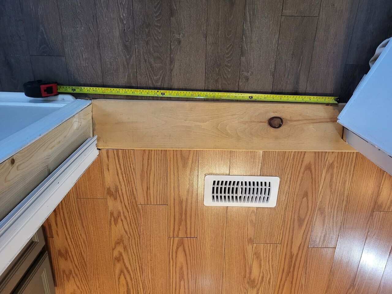Una stanza con pavimento in legno, una bocchetta di ventilazione e un metro a terra.