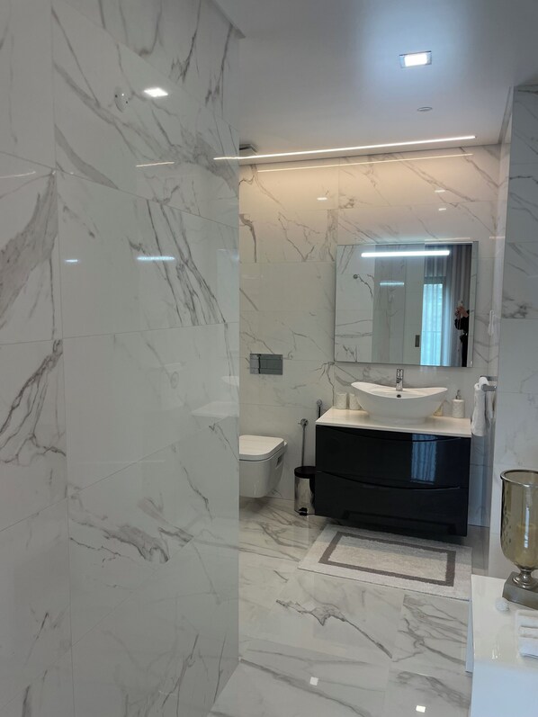 A modern bathroom with a marble floor, a black vanity, a white sink, and a large mirror.