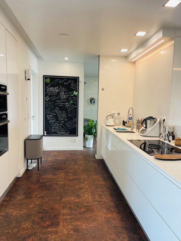 Una cocina moderna con armarios blancos, una pizarra con notas escritas a mano, un lavamanos y una encimera con varios utensilios de cocina.