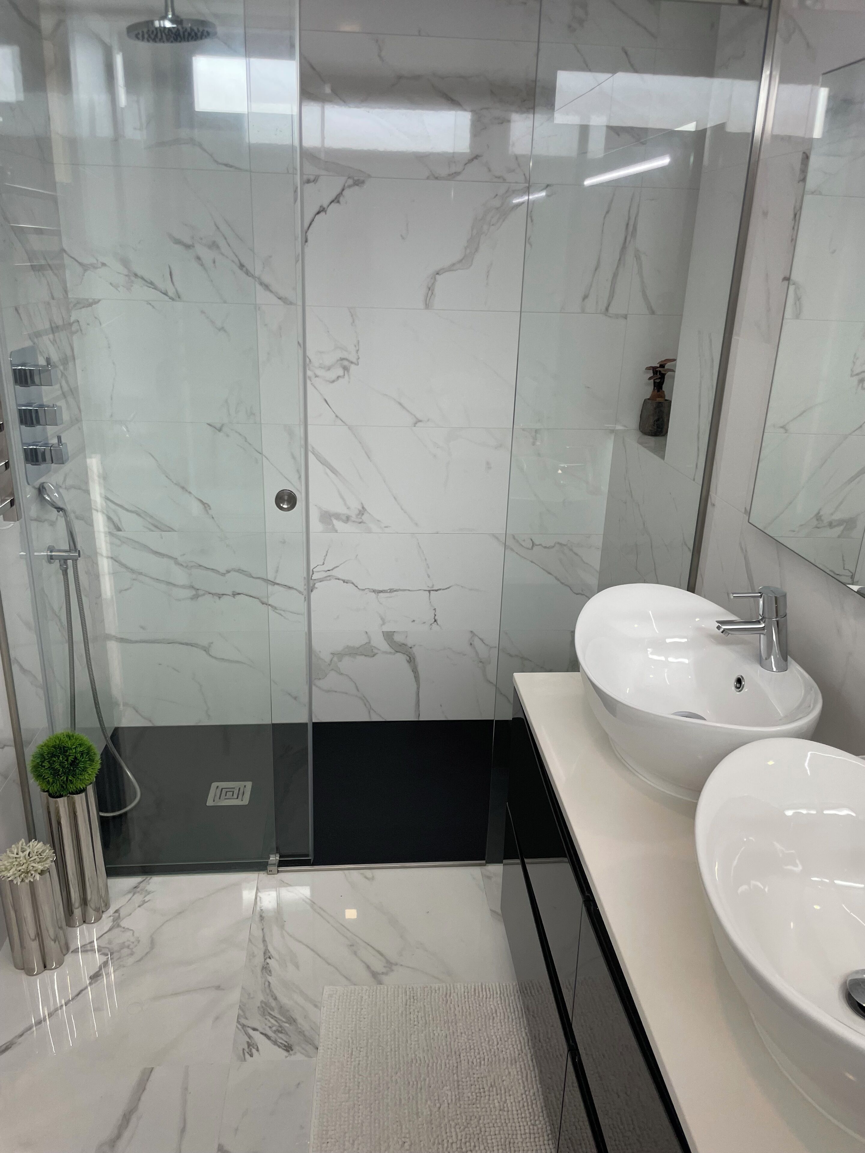 Un baño moderno con ducha de vidrio, lavabo blanco y un espejo grande.