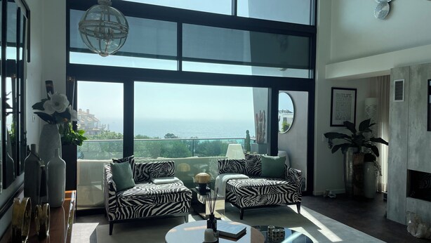 Un salon spacieux doté d’une grande fenêtre offrant une vue panoramique, de deux canapés à motifs zébrés, d’une table basse ronde et d’un lustre moderne.