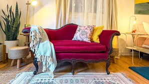 En hyggelig stue med en rød sofa, et rundt bord, en potteplante og en lampe.