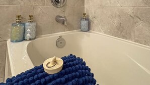 Et badeværelse med beige fliservægge, et hvidt badekar og en blå bademåtte med struktur.