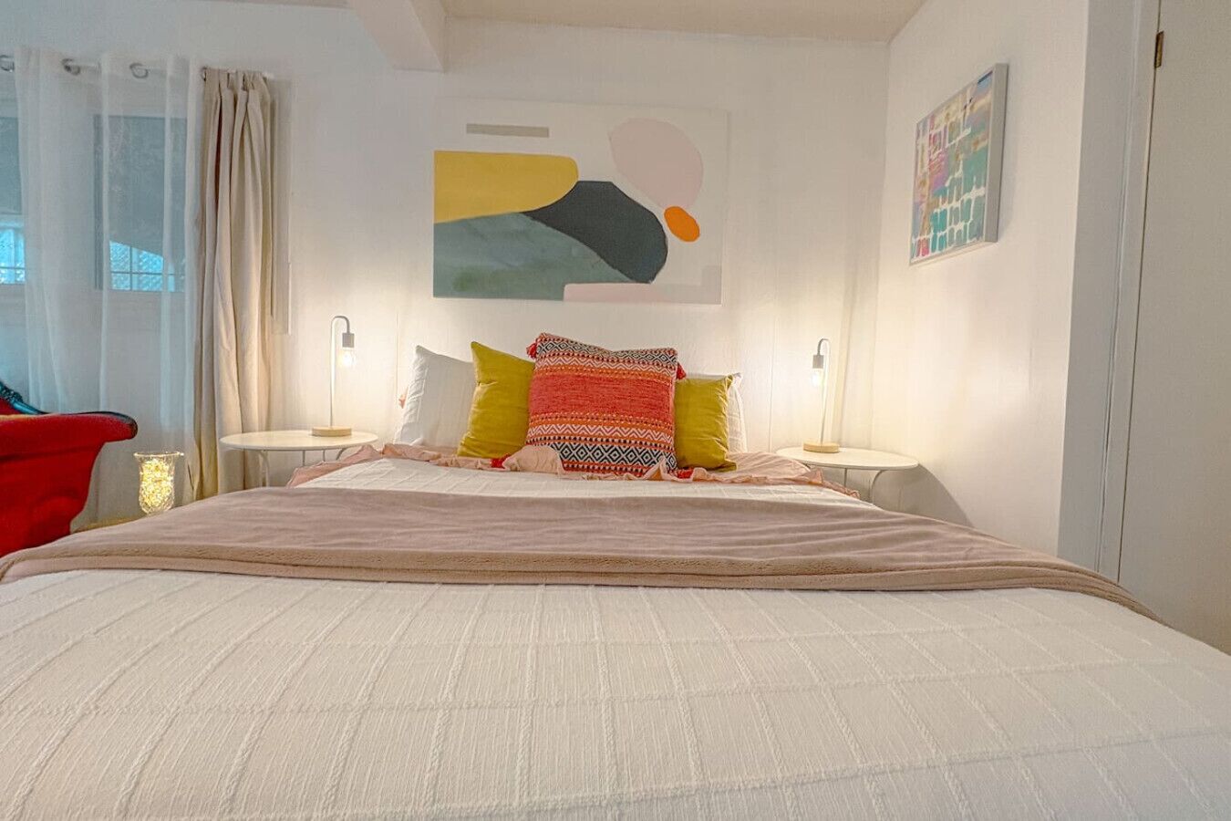 Un dormitorio con una cama grande, dos mesitas de noche, una silla roja y una obra de arte en la pared.