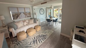 A spacious living room with a large sofa, a dining area with a round table, and a view of the outdoors.