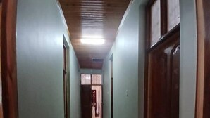 Un pasillo estrecho con paredes verde claro y techo de madera. Hay puertas a ambos lados y una puerta al final del pasillo.