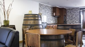Un comedor con una mesa redonda de madera y sillas, un sofá de cuero negro y dos barriles de madera.