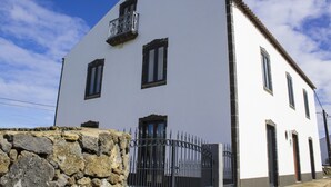 Un edificio blanco con un muro de piedra en primer plano, que incluye una reja metálica y un balcón.