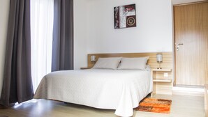 Un dormitorio con cama, cortinas, una obra de arte en la pared, una mesita de noche y una puerta de madera.