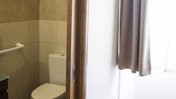A bathroom with a toilet, a shower area, and a wooden bench.