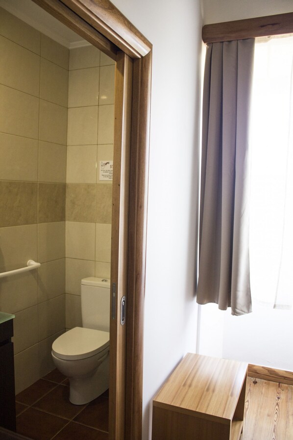 A bathroom with a toilet, a shower area, and a wooden bench. - Casa Lagar de Pedra T3 (Santa Cruz da Graciosa)