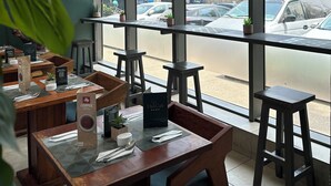 A cafe with wooden tables and chairs, large windows offering a view of the street and parked cars. - Easy Stay at the Lennox  (Accra)