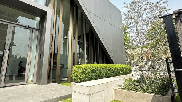 A modern building with large glass windows, a sloped roof, and a landscaped area with grass and bushes. - Easy Stay at the Lennox  (Accra)