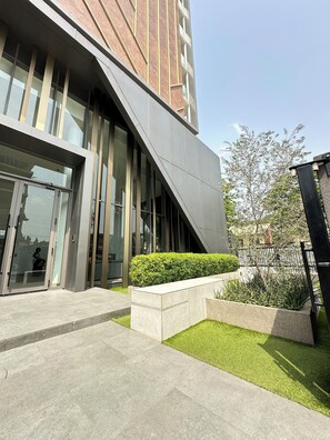 Een modern gebouw met grote glasramen, een schuin dak en een aangelegde tuin met gras en struiken.
