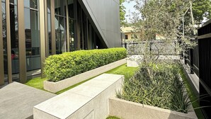 A modern building with large windows, a landscaped garden with grass and shrubs, and a concrete bench. - Easy Stay at the Lennox  (Accra)