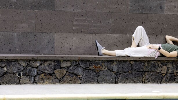 Una persona recostada sobre un borde de piedra junto a una pared de hormigón.
