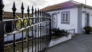 Un edificio blanco con techo de tejas, entrada protegida por una reja y macetas con plantas.