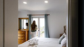 Une chambre à coucher avec un lit, une commode en bois, un miroir et une fenêtre avec des rideaux.