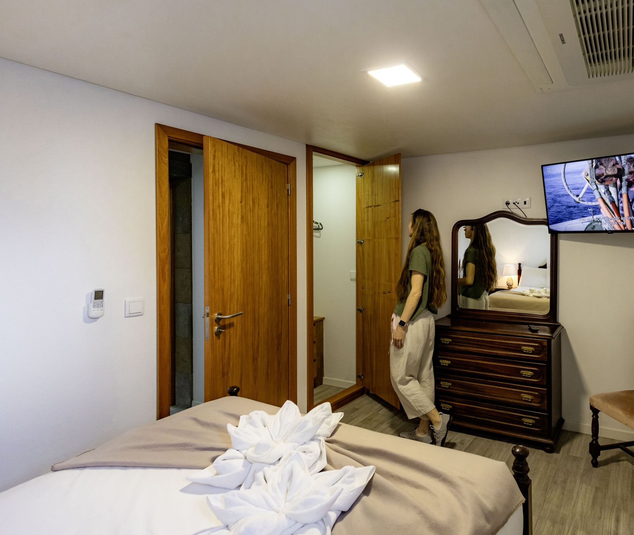 Habitación de hotel con cama, armario de madera, cómoda, televisor y baño visible a través de una puerta abierta.