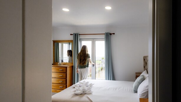 Une chambre à coucher avec un lit, une commode en bois, un miroir et une fenêtre avec des rideaux.