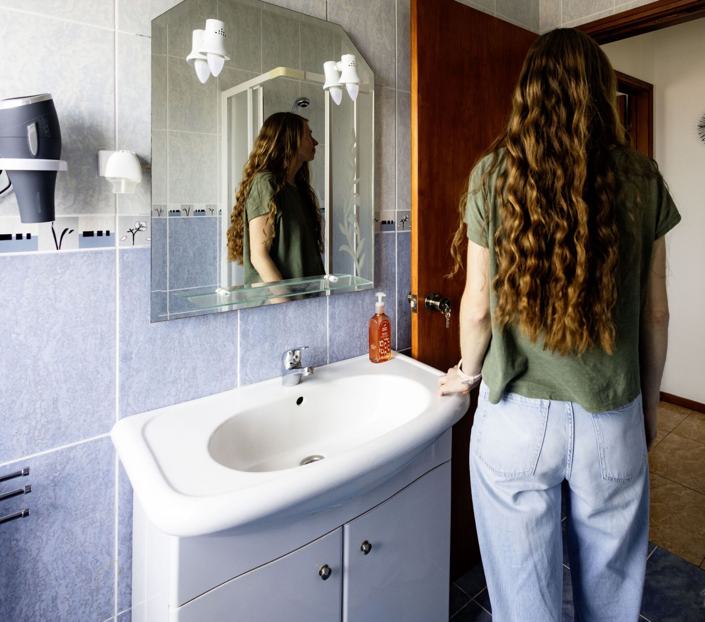 Une salle de bain avec un lavabo blanc, un miroir et un sèche-cheveux fixé au mur.
