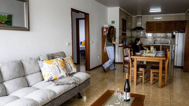A living room with a sofa, a dining table, and a kitchen area with wooden cabinets and a refrigerator.