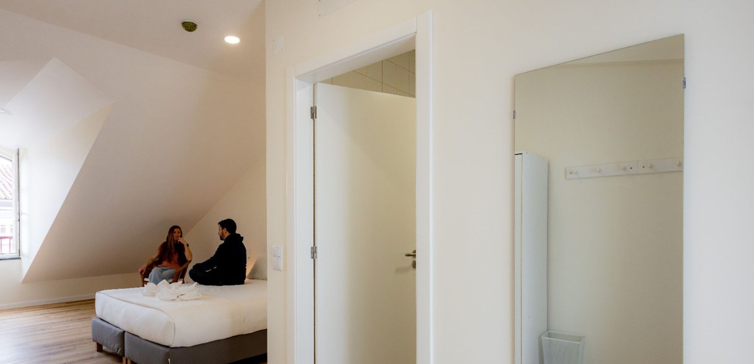 A bedroom with a sloped ceiling, a bed, a door, and a wall-mounted light fixture.