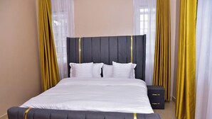 A neatly made bed with white linens and a dark headboard, flanked by yellow curtains. - Lux Suites comfy Homestays Nakuru (Nakuru)