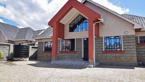 A two-story house with a red and beige exterior, a tiled roof, and a paved driveway. - Lux Suites comfy Homestays Nakuru (Nakuru)