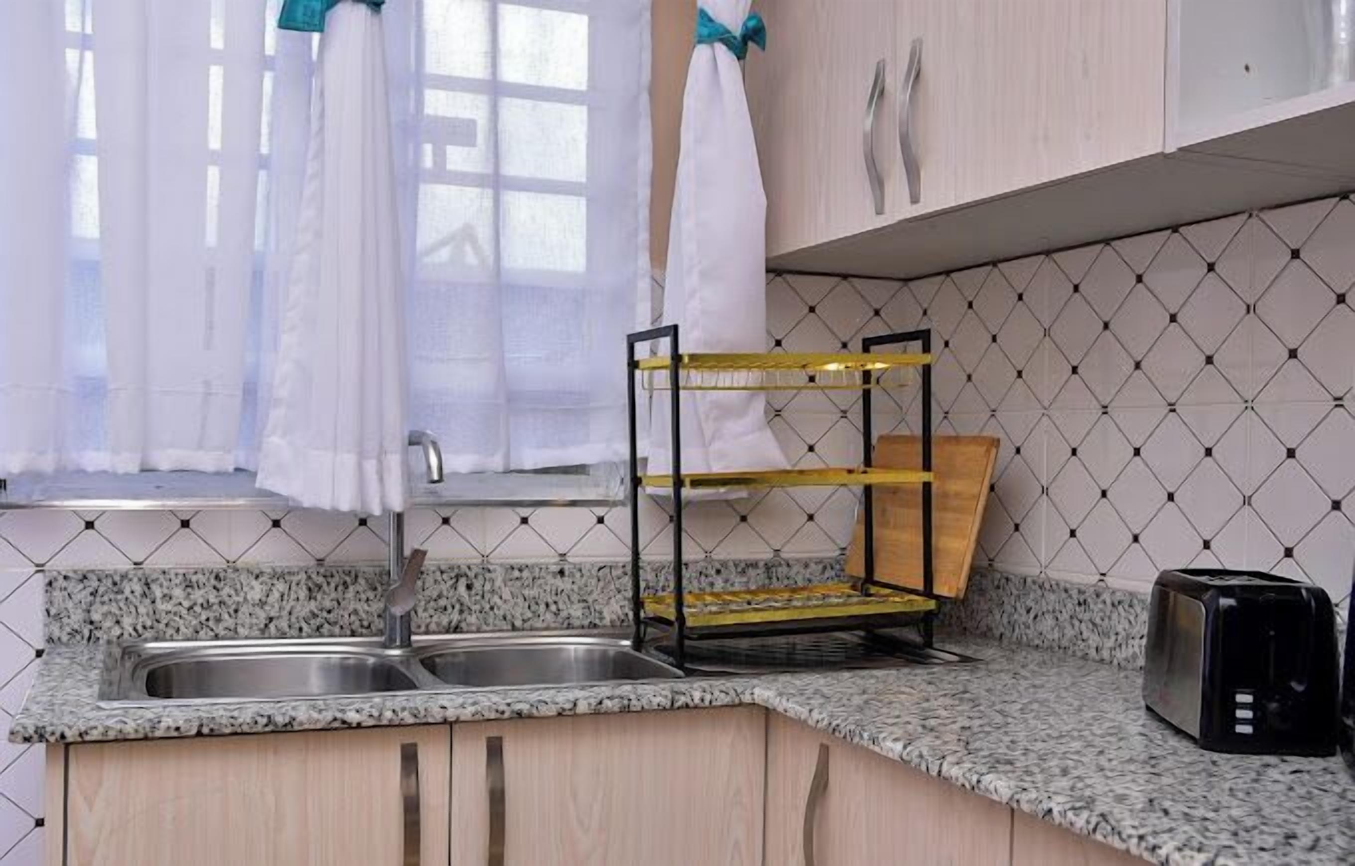 A kitchen with granite countertops, a double sink, a wooden cutting board, and a black toaster.
