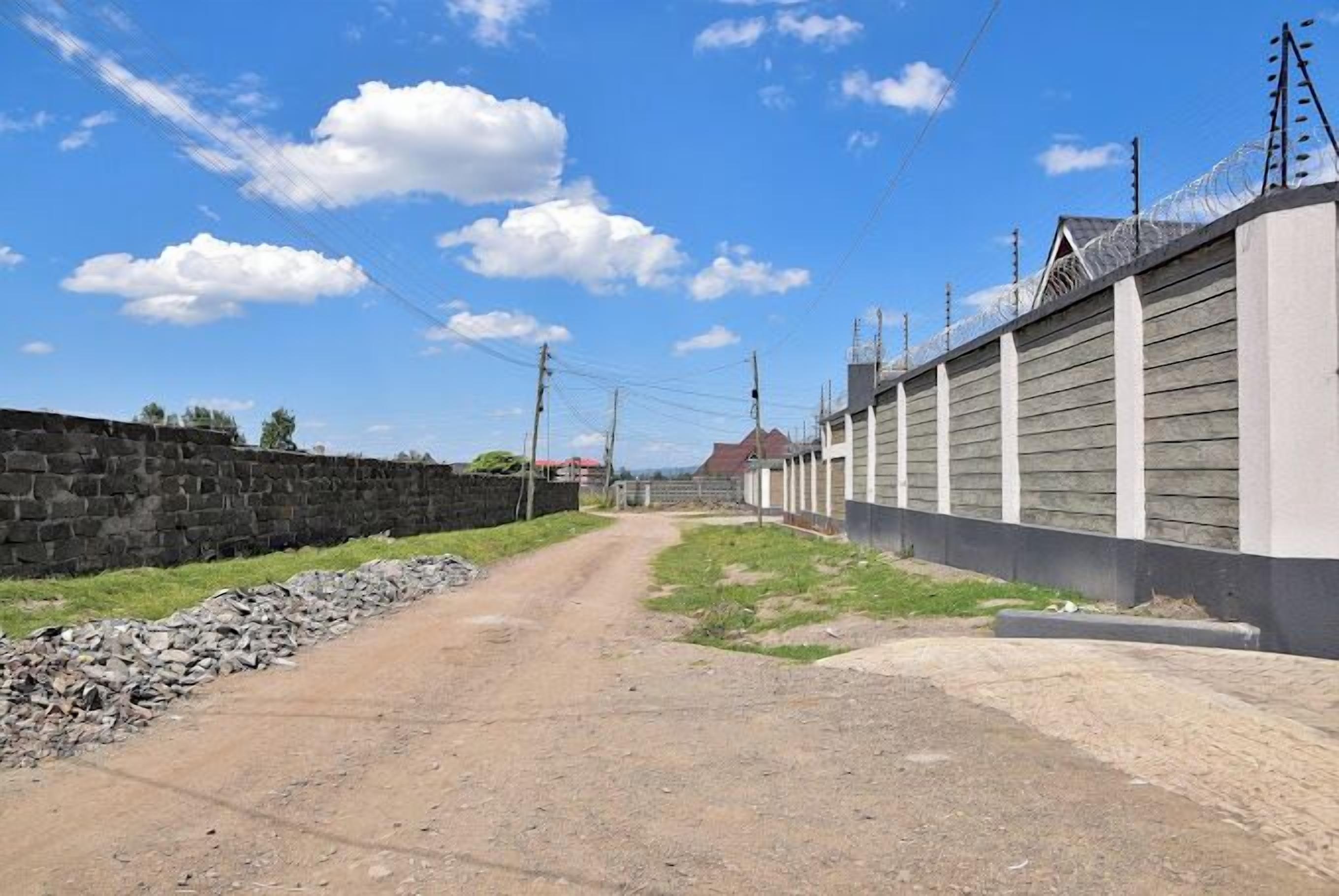 A dirt road flanked by a stone wall and a wooden fence with barbed wire.