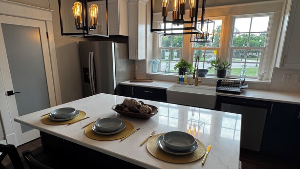 Une cuisine moderne dotée d’un îlot central, d’appareils électroménagers en acier inoxydable et de luminaires suspendus.