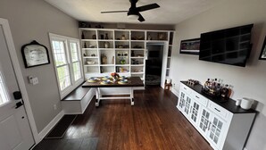 Une cuisine avec une table à manger pour six personnes, un meuble blanc avec des portes en verre, un ventilateur de plafond et un téléviseur fixé au mur.