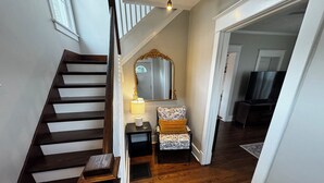 Un escalier avec des marches en bois et une rampe, menant à un palier où se trouvent une lampe et un fauteuil à motifs.