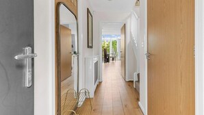 Un pasillo con suelo de madera, paredes blancas y una puerta a la derecha.