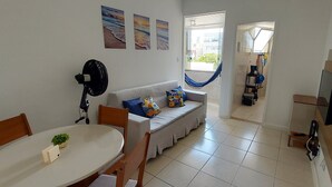 A compact living space with a dining area, a sofa with cushions, a hammock, and a TV mounted on the wall. - COPIT0105 - Edifício Cidade de Caravelas (Salvador)