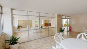 A spacious indoor area with a large sliding glass door leading to an outdoor patio. There are white plastic chairs and a round table in the center. - COPIT0105 - Edifício Cidade de Caravelas (Salvador)