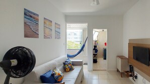 A hallway with a sofa, a fan, and a TV mounted on the wall. - COPIT0105 - Edifício Cidade de Caravelas (Salvador)