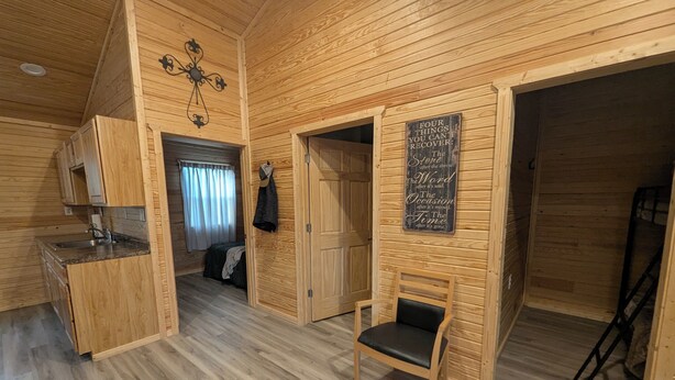 A cozy wooden cabin interior with a kitchen area, a dining table with chairs, and a chalkboard with inspirational quotes. - Wichita's Spring Lake RV Resort (Halstead)
