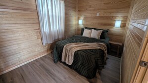A wooden cabin room with a bed, curtains, and two wall-mounted lights. - Wichita's Spring Lake RV Resort (Halstead)