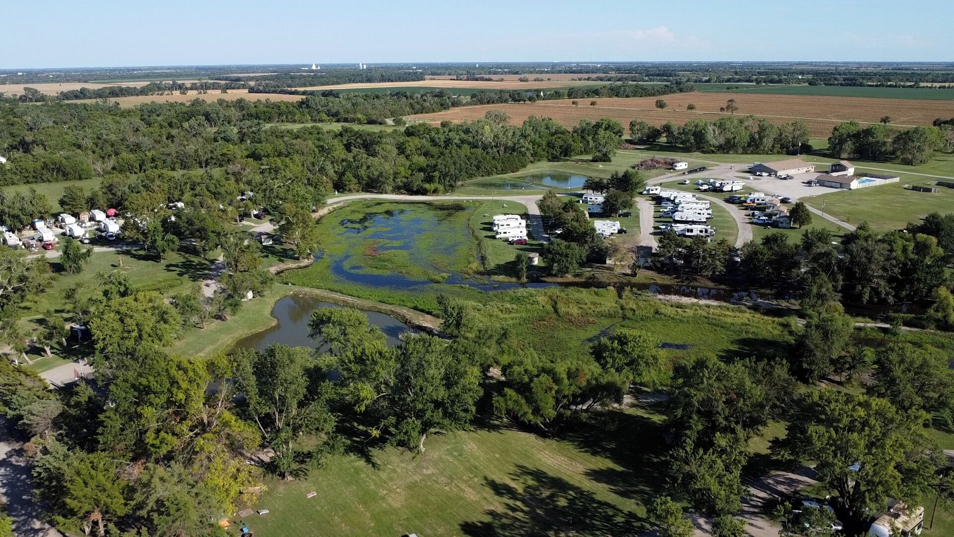Vista aérea de um camping com trailers, um lago e vegetação ao redor.