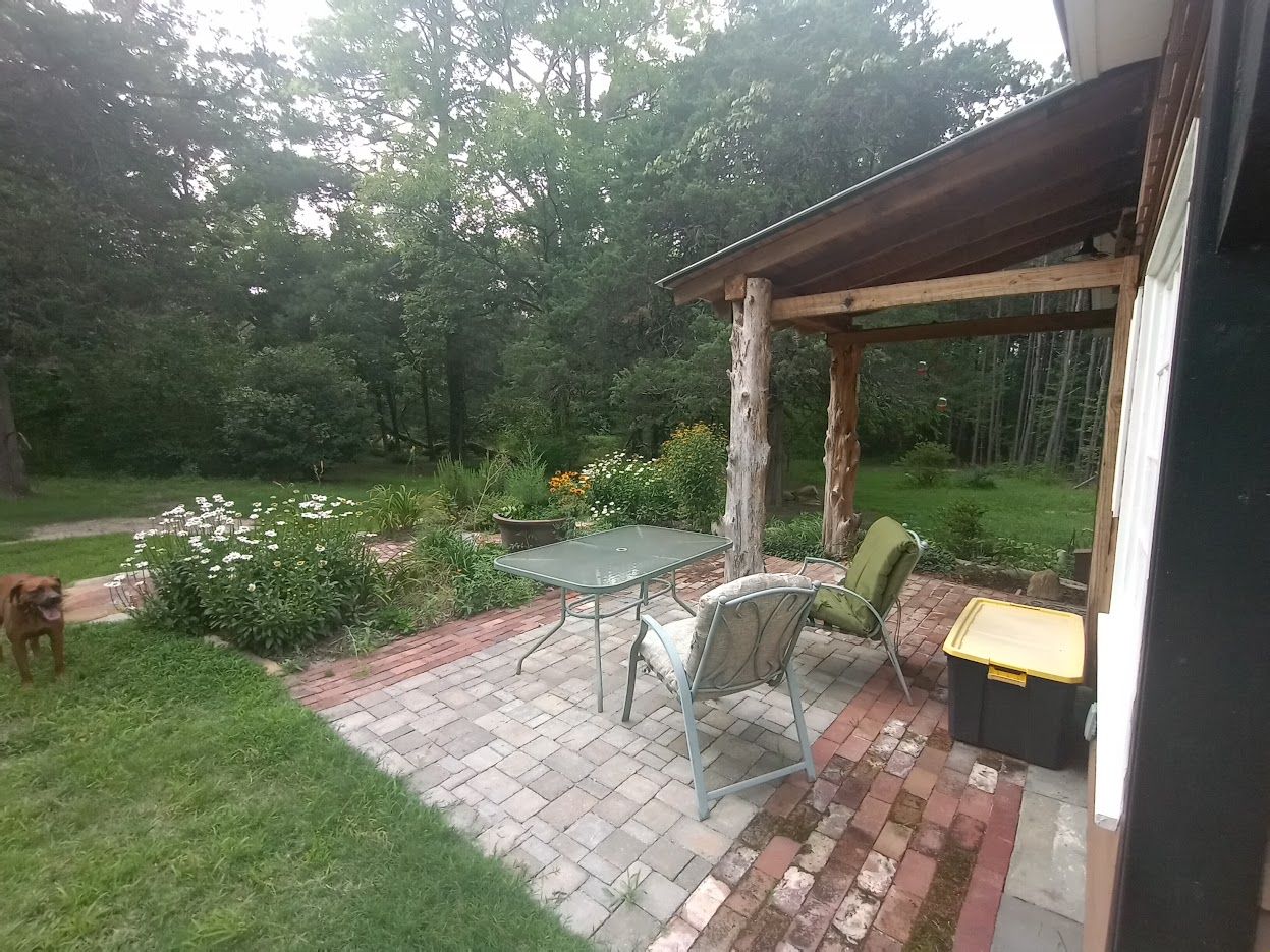 Un patio con una mesa y sillas, rodeado por un jardín con flores y césped.