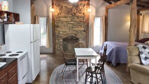 A rustic kitchen with a stone fireplace, wooden ceiling beams, and a dining area with a table and chairs. - Charming cabin get away w/ walk-in shower, kitchenette,  AC/heat, WiFi (Henderson)