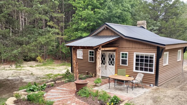 A small wooden cabin with a patio, surrounded by a garden and trees. - Charming cabin get away w/ walk-in shower, kitchenette,  AC/heat, WiFi (Henderson)