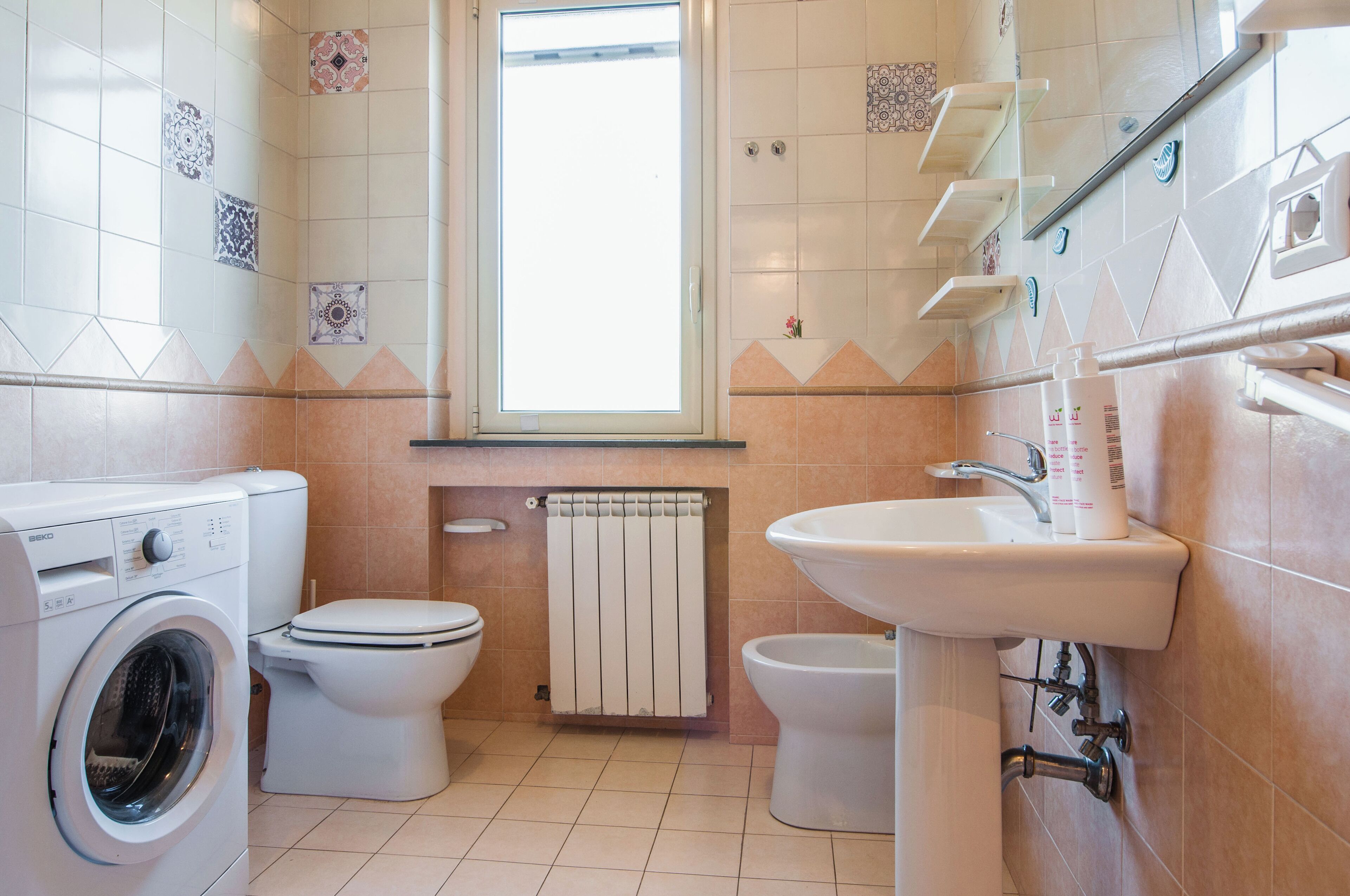 Une salle de bain équipée d’un lave-linge, de deux toilettes, d’un lavabo et d’une fenêtre.