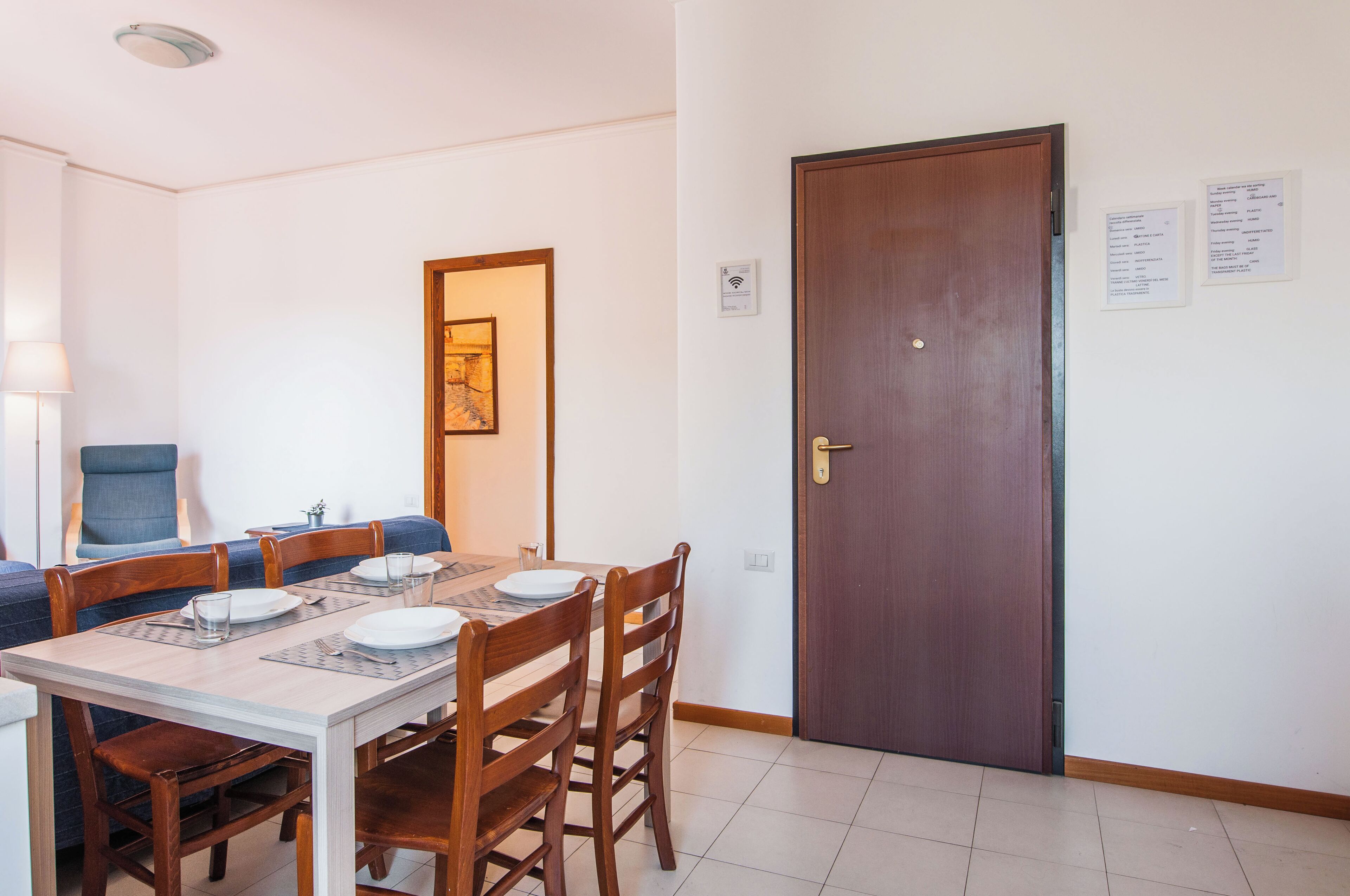 Un coin repas avec une table en bois dressée pour quatre personnes, un canapé bleu et une porte en bois dotée d’une serrure.