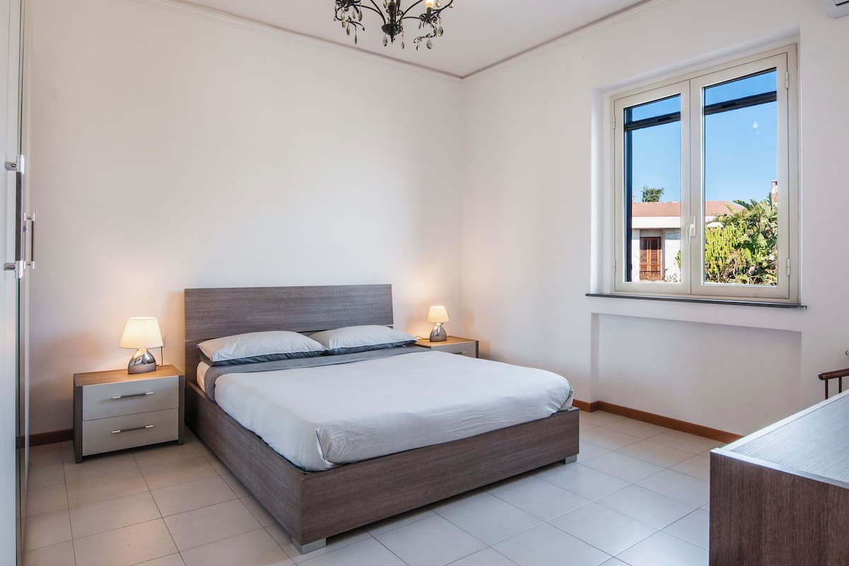 Ein Schlafzimmer mit Bett, Nachttischen, einer Chandelüster und einem Fenster mit Blick.