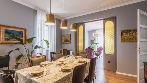 Un comedor con una mesa dispuesta para cuatro personas, rodeada de sillas, y vista a un salón de comidas por un vano de puerta.
