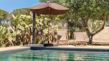 Een buitenzwembad, parasols bij het zwembad en ligstoelen